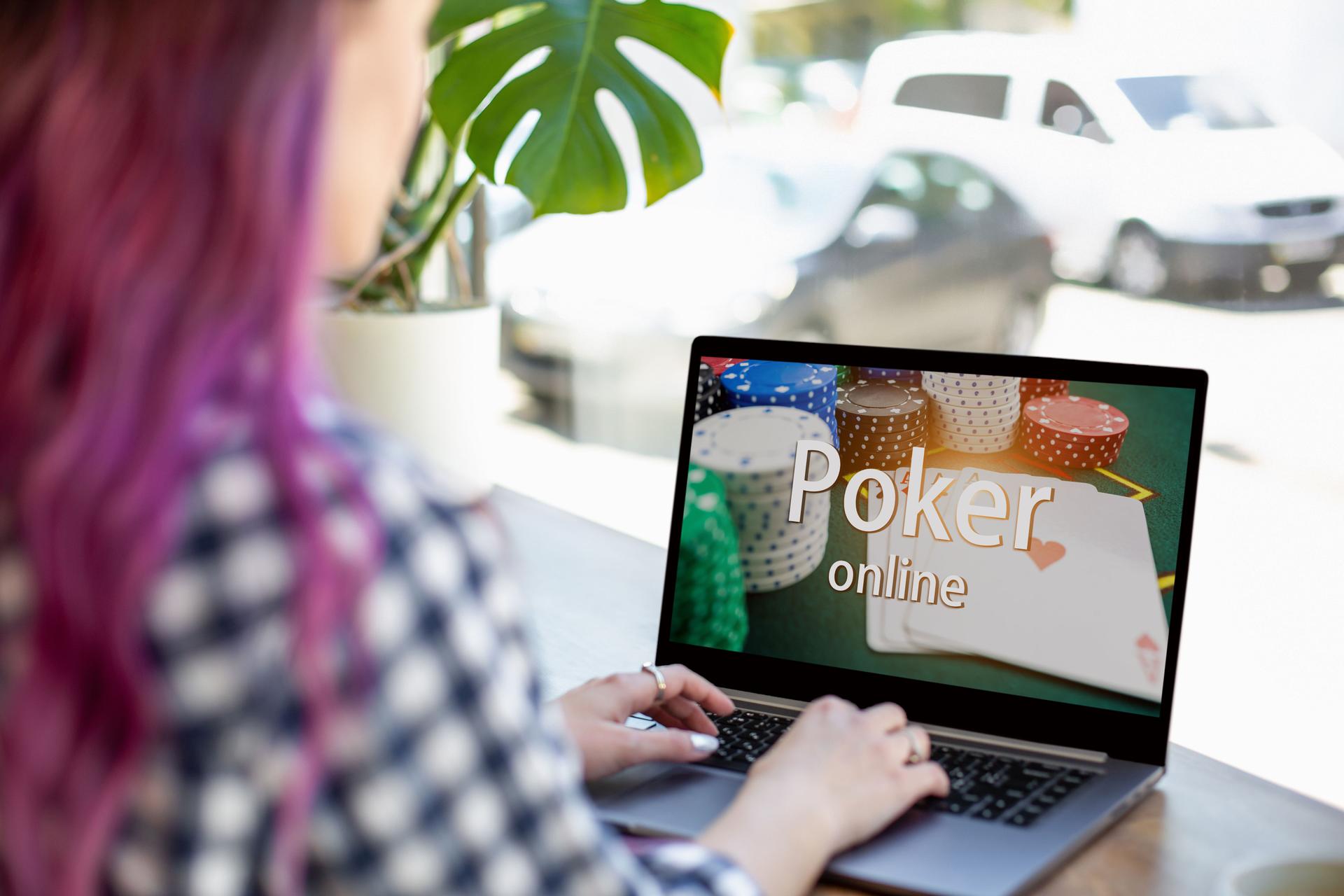 Back view of a young pink hair woman keyboarding on laptop computer with poker online on a screen while sitting in cafe