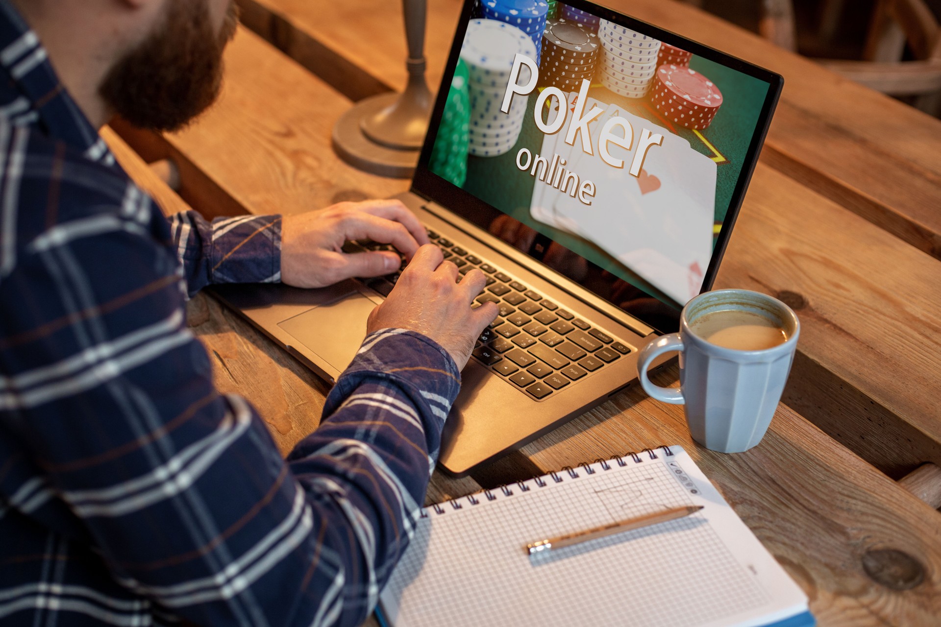 Young man playing poker via netbook during work-break in coffee shop, male sitting in front open laptop computer.